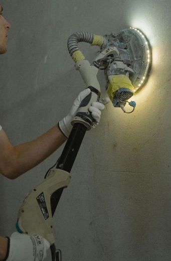 A person is using a sander on a wall with a light on it.
