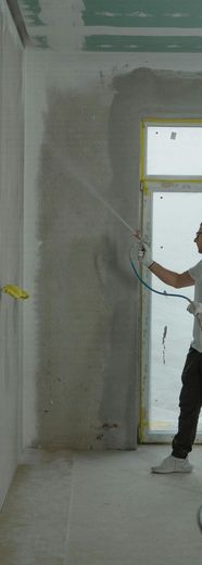 A man is spraying paint on a wall in a room.