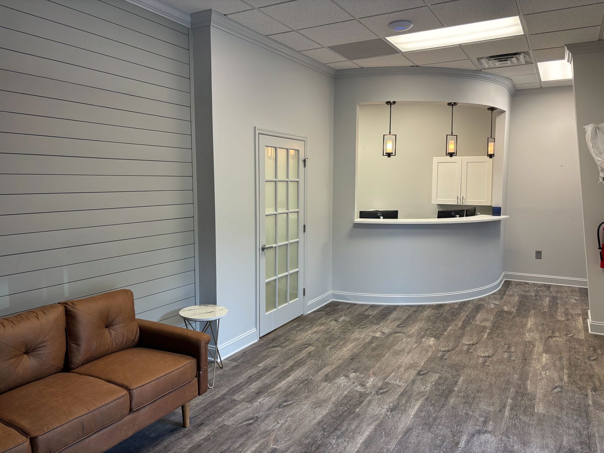 Reception area with brown sofa, curved counter, and wood-look flooring. Light gray walls.
