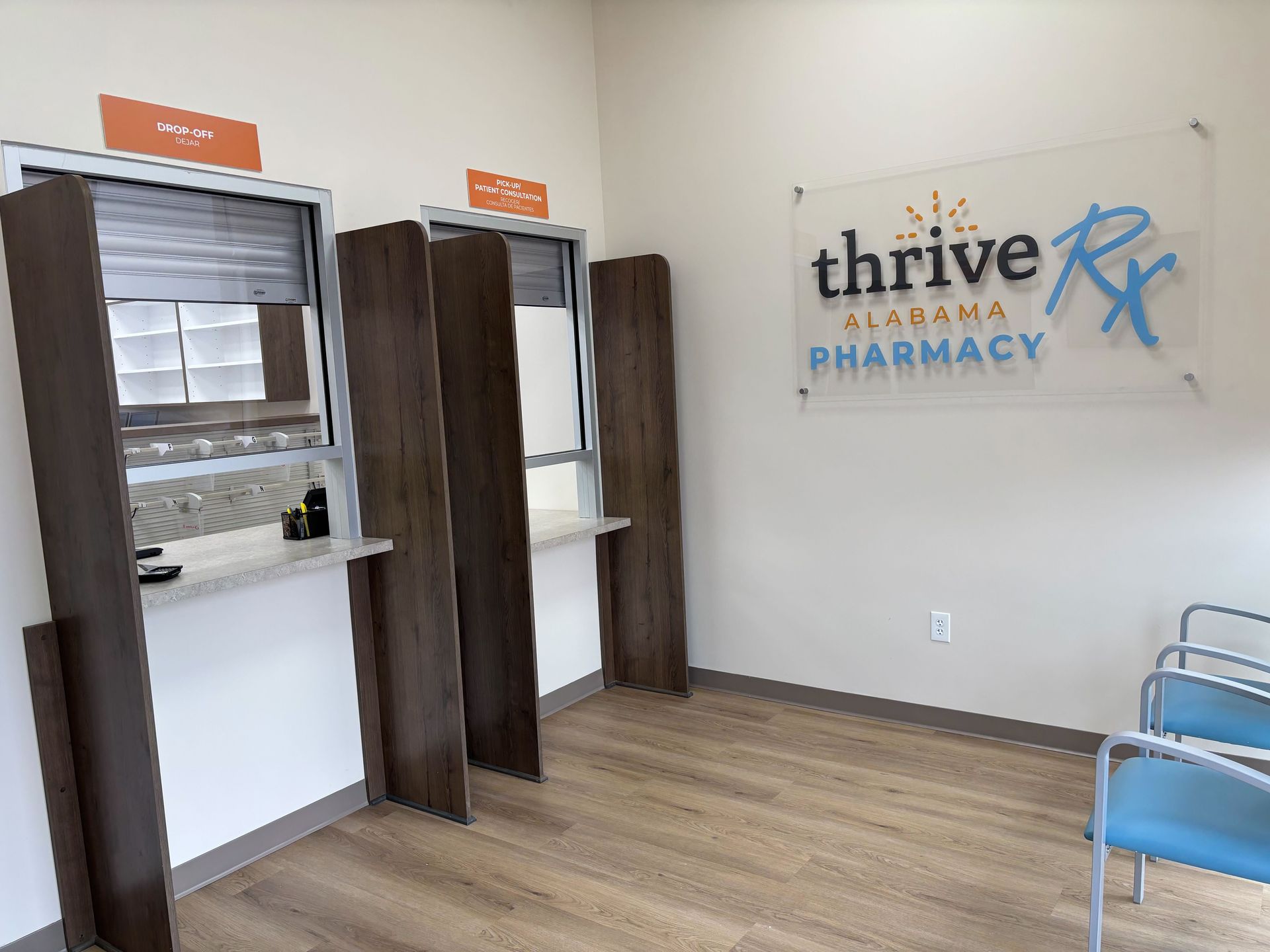 Pharmacy interior with two service windows, waiting chairs, and a sign that reads