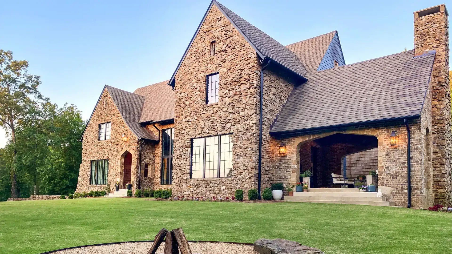A large stone house with a fire pit in front of it.