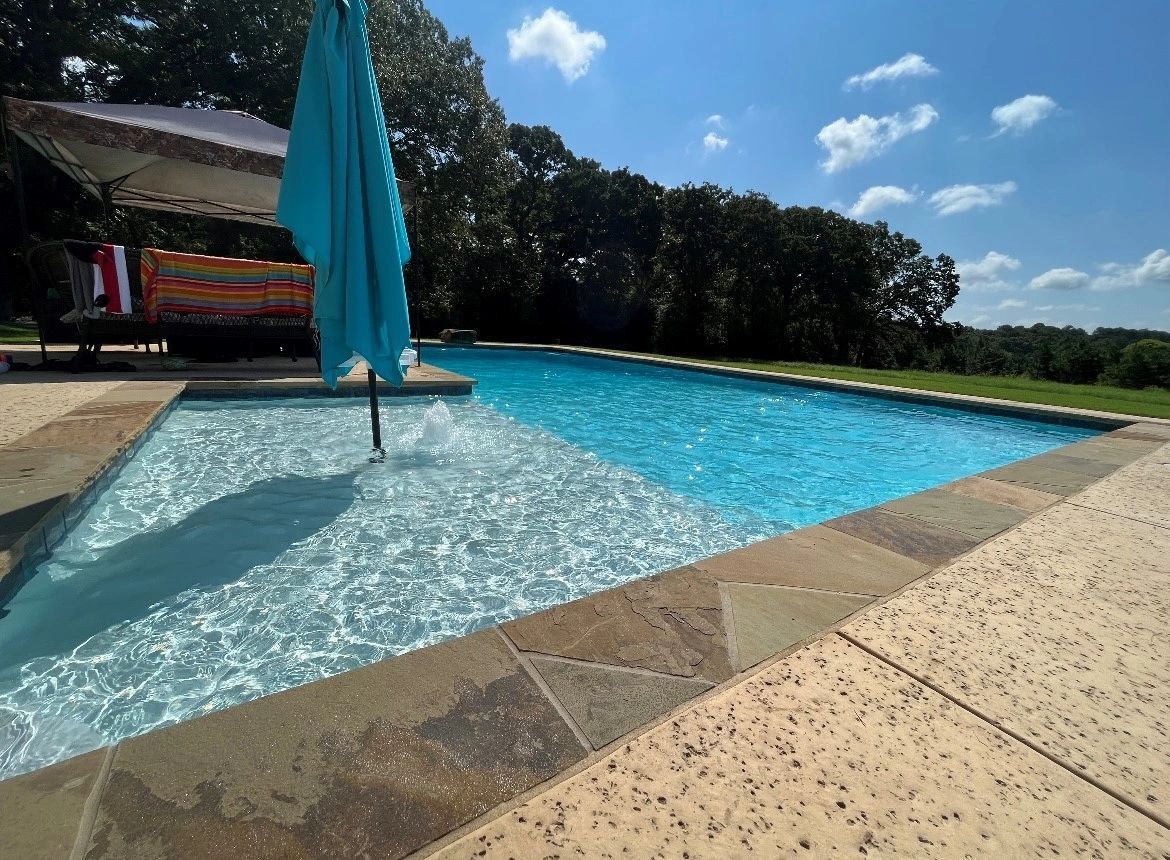 A large swimming pool with a blue umbrella on the edge