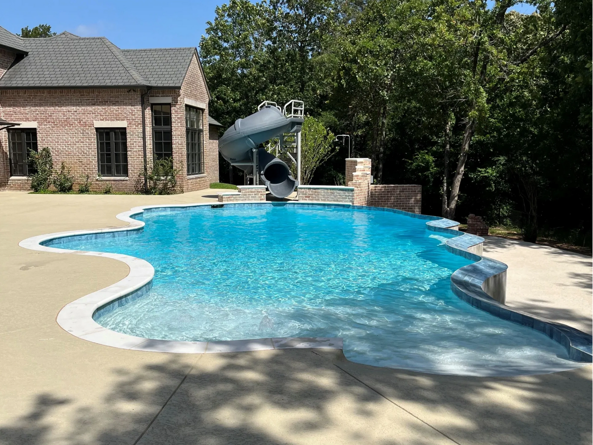 A large swimming pool with a slide in the backyard of a house.