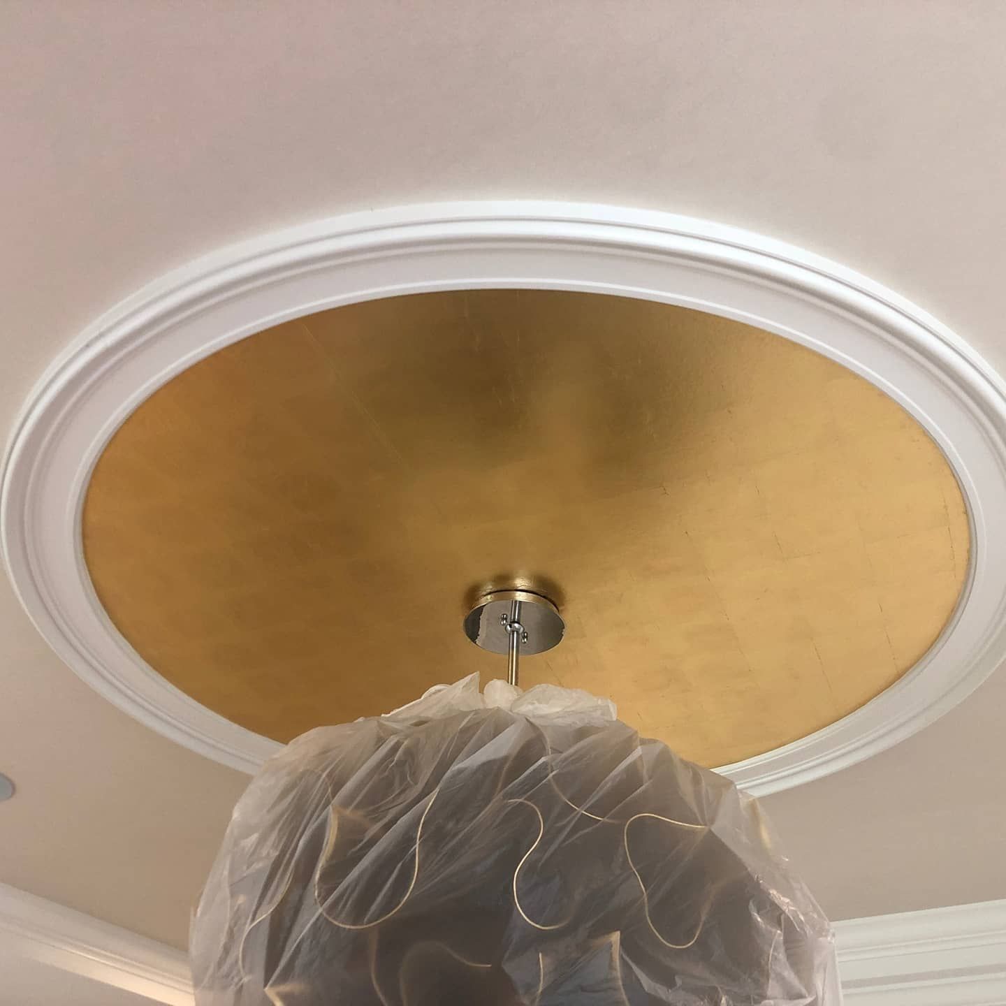Gold-painted ceiling medallion with white molding, a pendant light wrapped in plastic.