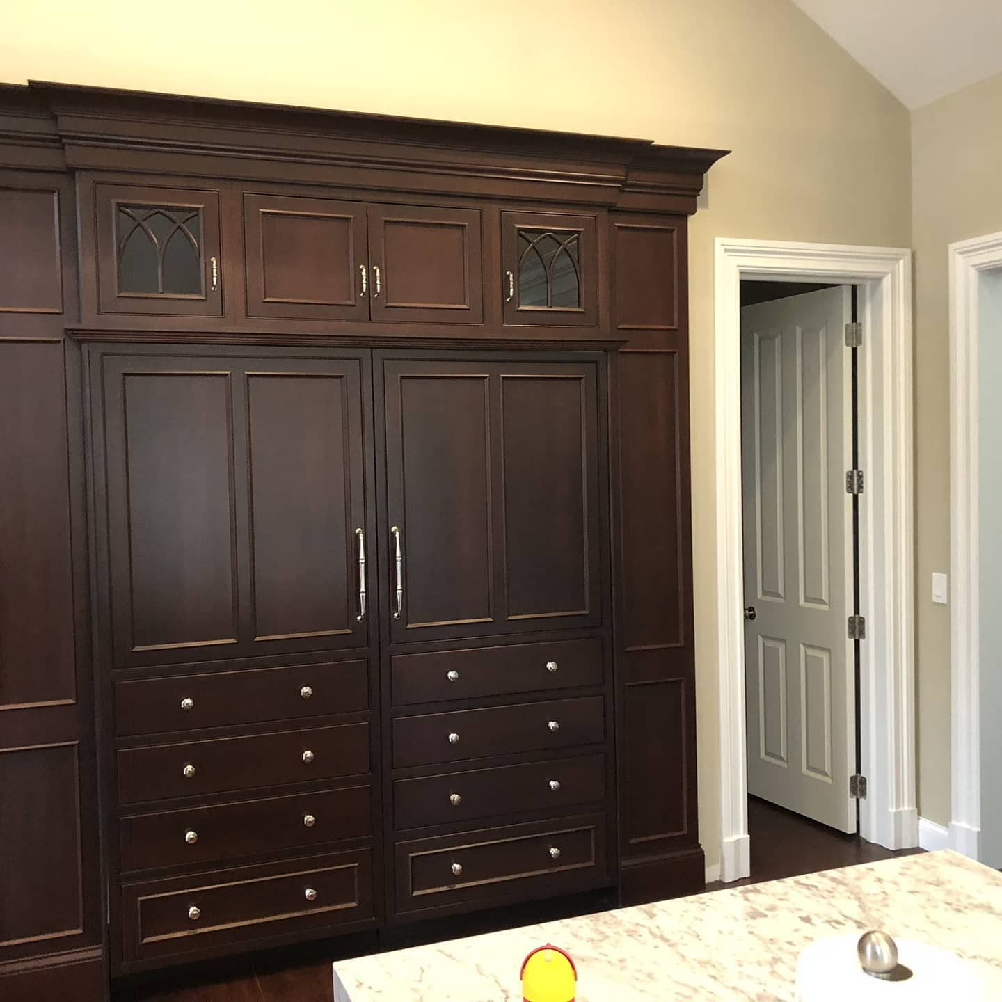 Dark wood kitchen cabinets with drawers and doors, built-in with a decorative top, beside a doorway.