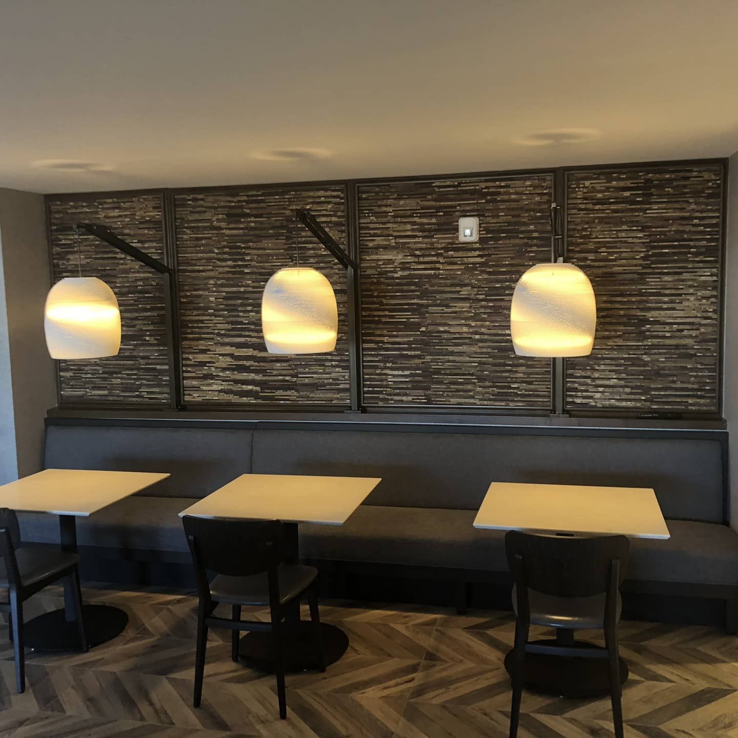 Restaurant booth with tables, chairs, and three pendant lights against a textured wall.