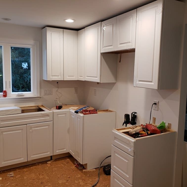 White kitchen cabinets installed in a room with a window and unfinished countertops.