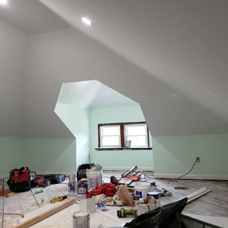 Attic room under construction with a window, tools, and paint. Light green walls, white ceiling, and a wood floor.