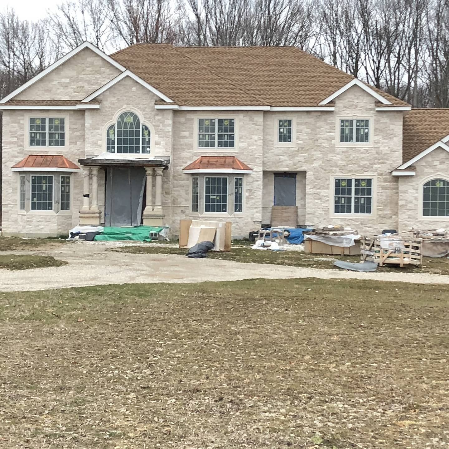 Two-story house under construction, light brick exterior, brown roof, multiple windows, front yard with construction debris.