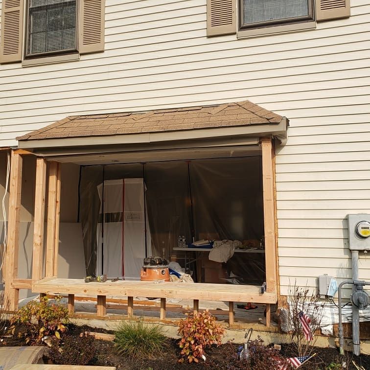 Exterior of a building with a porch under construction; unfinished wooden frame, tarp, and tool clutter.