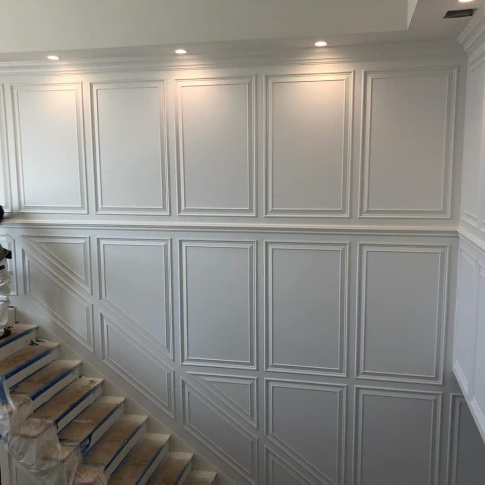 White paneled wall with recessed lighting above a staircase.