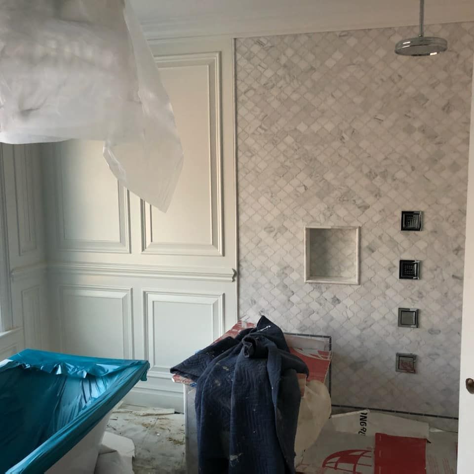 Bathroom under construction with marble tiled shower, white paneling, and a covered bathtub.