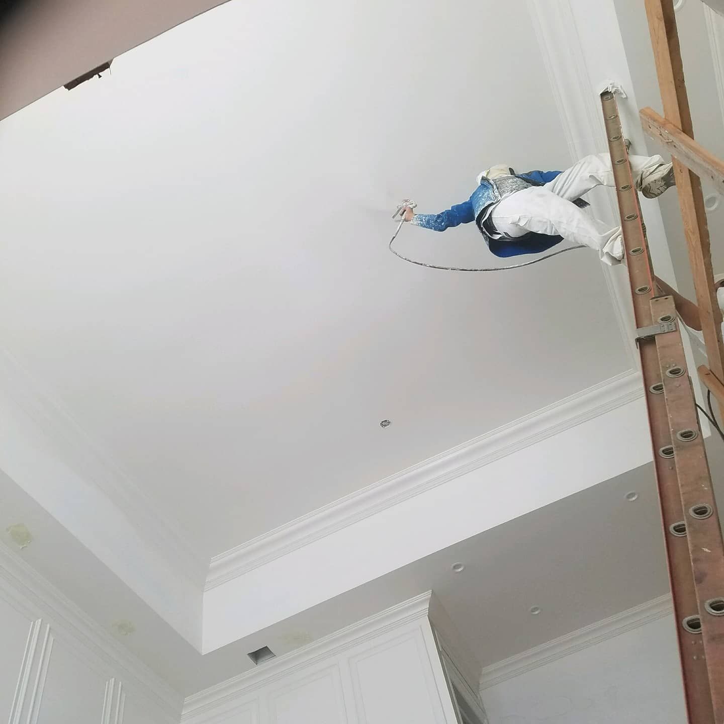 Person spraying paint on a white ceiling from a ladder.