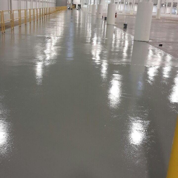 A shiny, gray industrial floor reflects overhead lights and pillars.