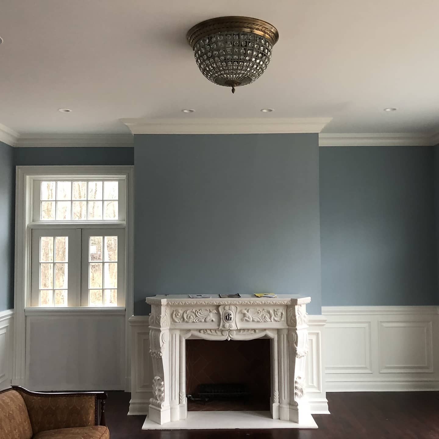 Blue-painted living room with white fireplace and trim, a crystal chandelier, and a window.