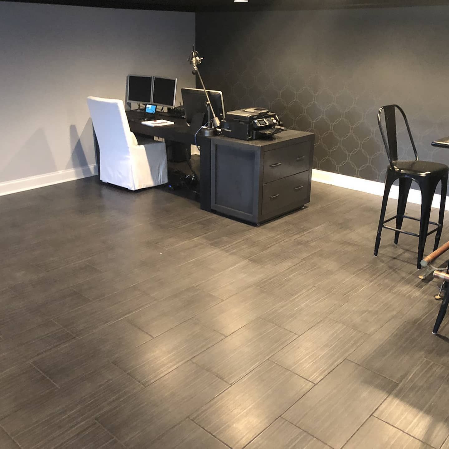 Dark gray tiled floor in home office setup, desk with monitors, file cabinet, and a chair.