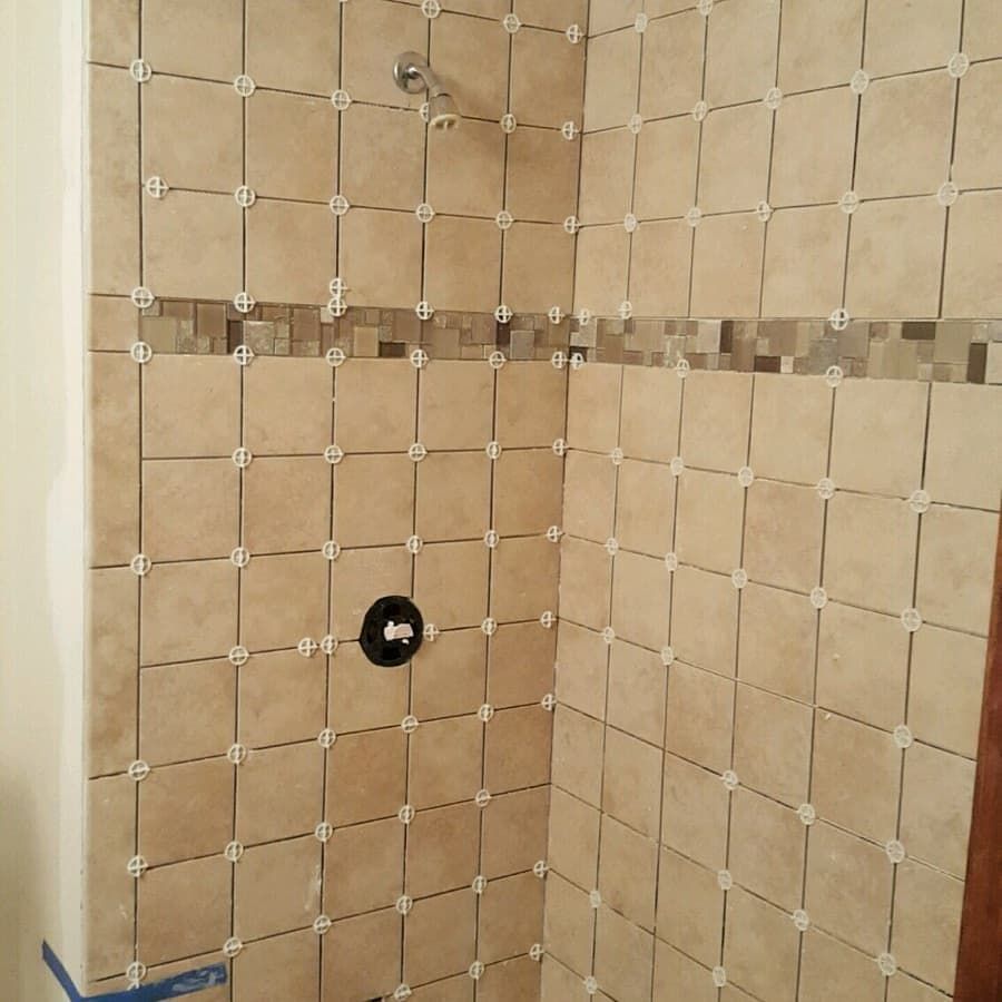 Shower stall with beige square tiles and a decorative border of smaller, mixed-color tiles.