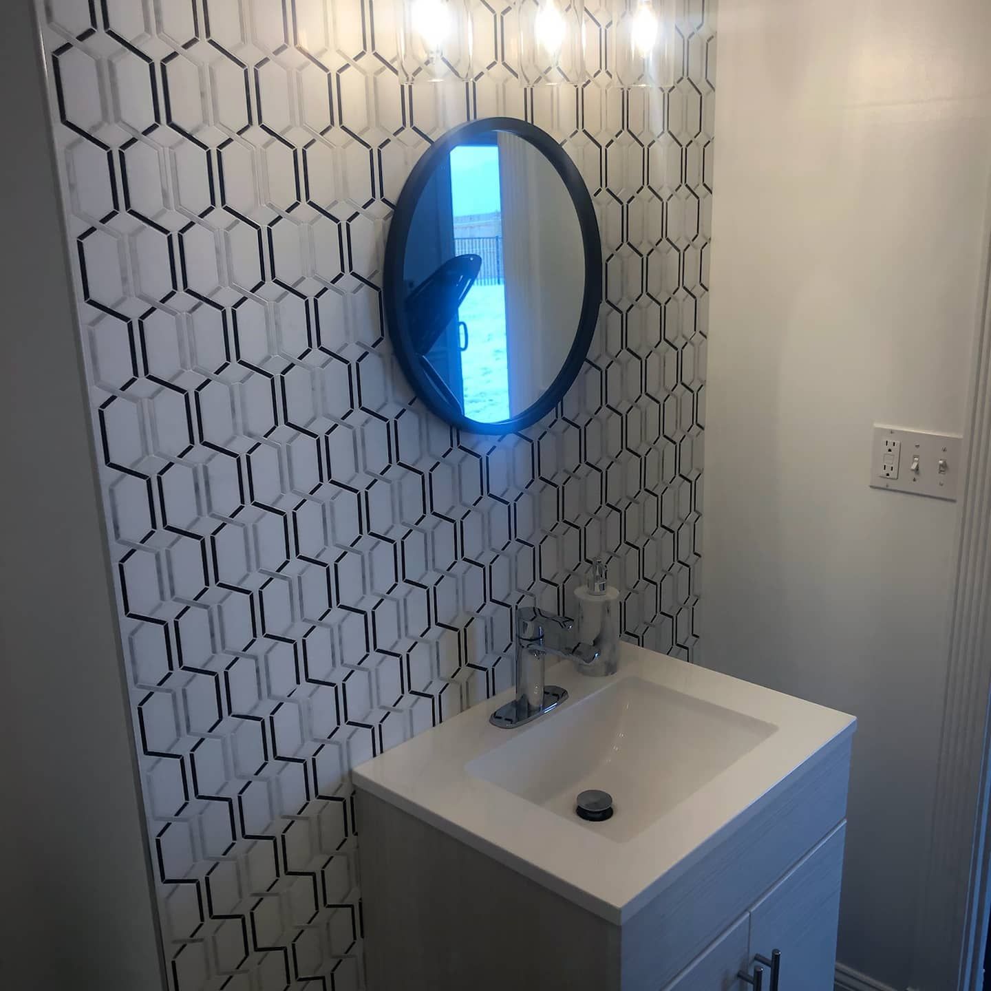 Bathroom with white vanity, black and white hexagon patterned wall, oval mirror.