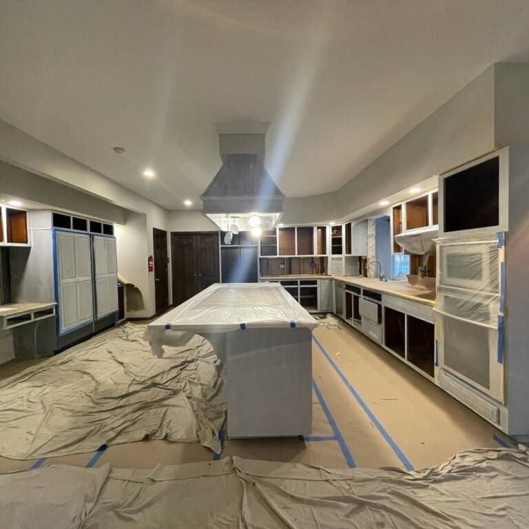 Kitchen remodel: cabinets and island being painted. Blue tape, drop cloths cover surfaces.