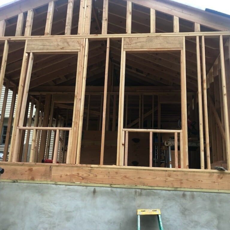 Wood frame construction of a house addition; two window frames visible.