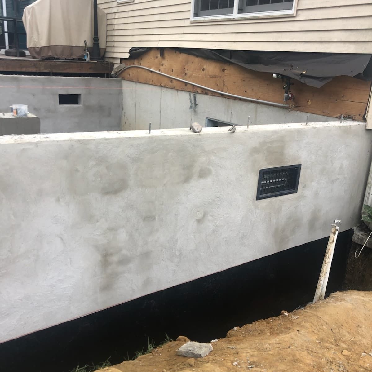 Concrete foundation wall under a building, black waterproof coating, excavated ground.
