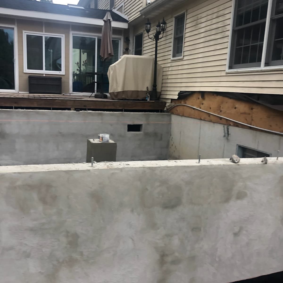 Exterior view of a newly constructed concrete structure beneath a house, with an exposed deck above and a section of the house visible.
