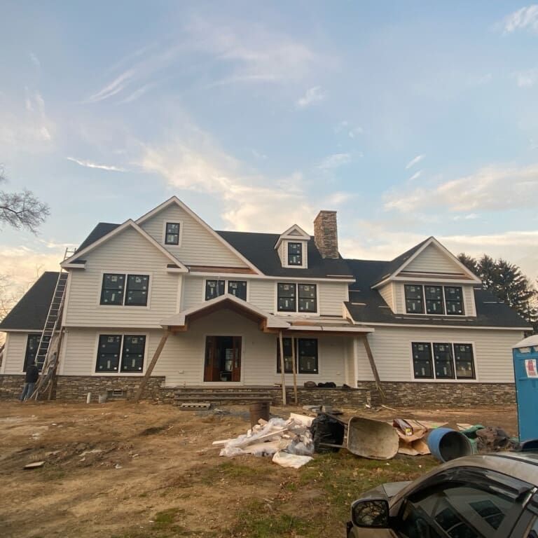 Two-story house under construction with white siding, dark roof, stone accents, and several windows.
