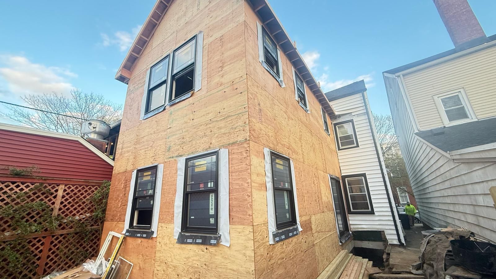 Two-story house under construction, with exposed wood siding and installed windows; sky in background.
