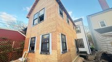 Two-story house under construction, with exposed wood siding and installed windows; sky in background.