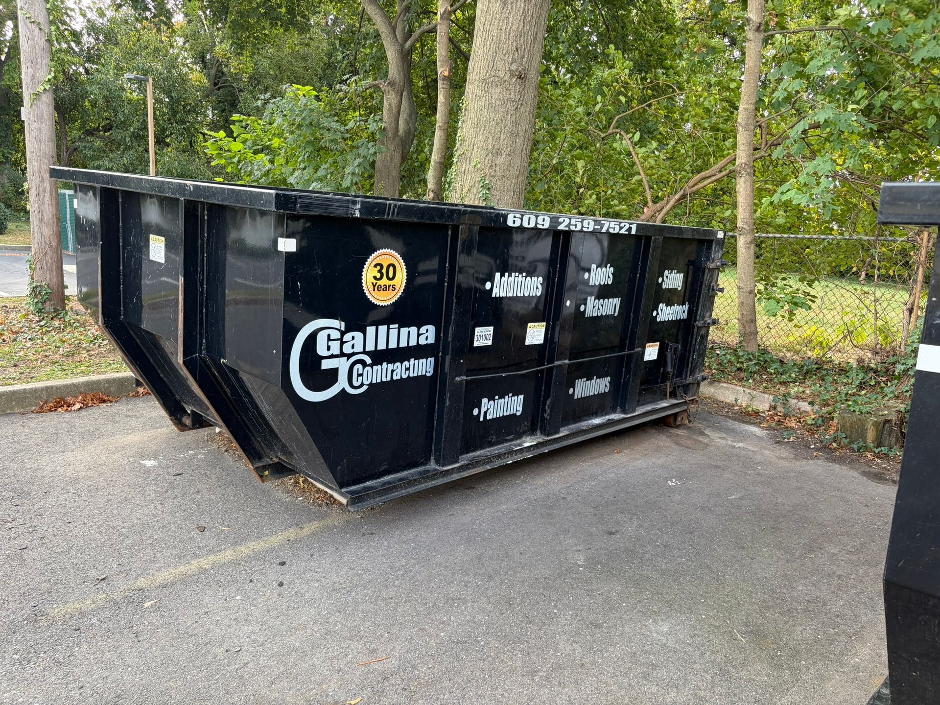 Black construction dumpster parked on asphalt, labeled 