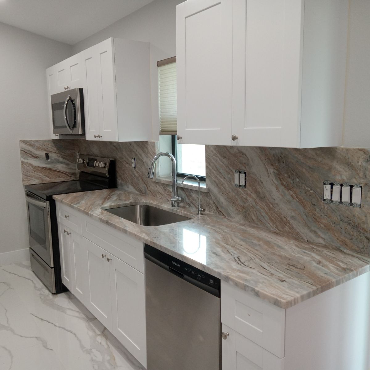 White kitchen cabinets with granite countertops, stainless steel appliances, and a window.