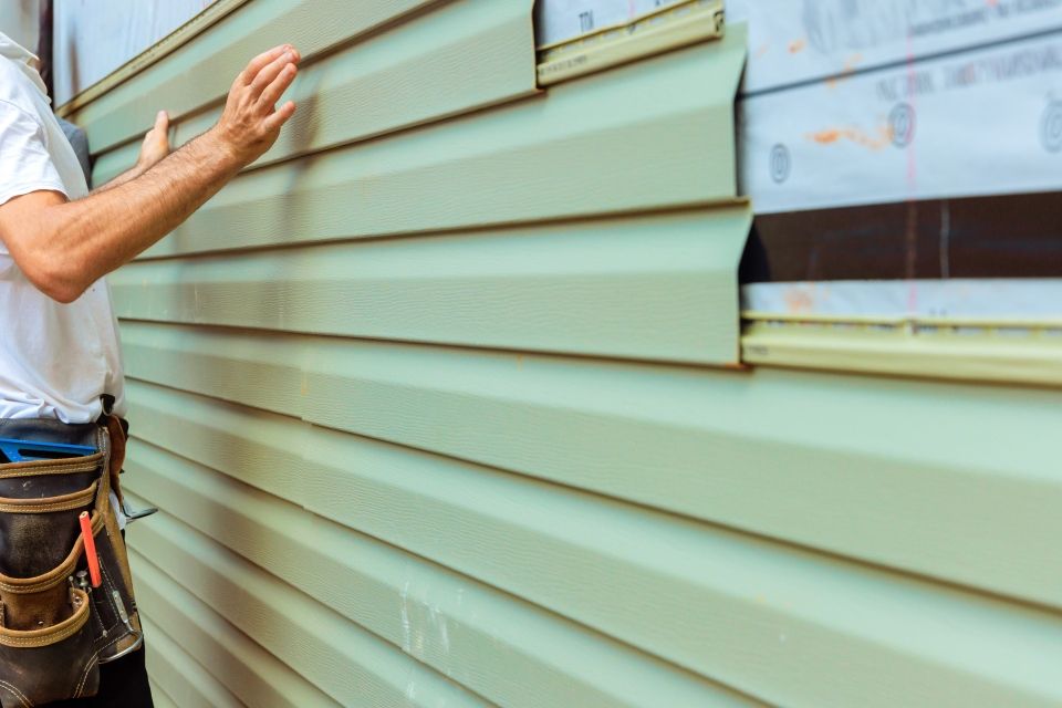 A person installs light green vinyl siding on a building's exterior wall.