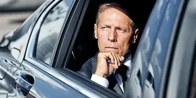 A man in a suit and tie is sitting in a car looking out the window.