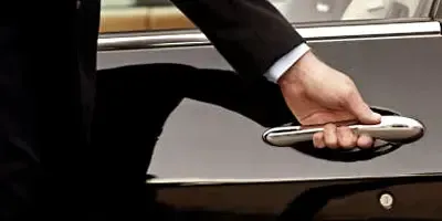 A man in a suit is opening the door of a black car.