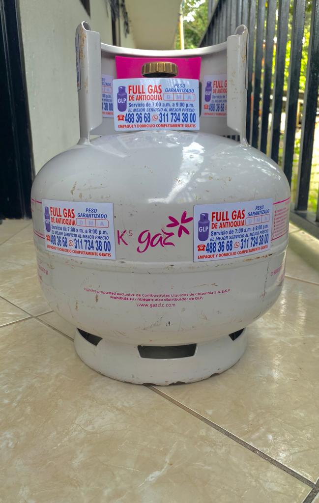 Una bombona de gas se encuentra sobre un suelo de baldosas, al lado de una valla.