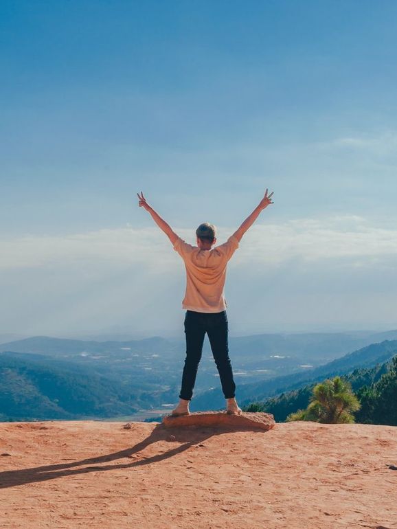 A woman is standing on top of a hill with her arms outstretched.