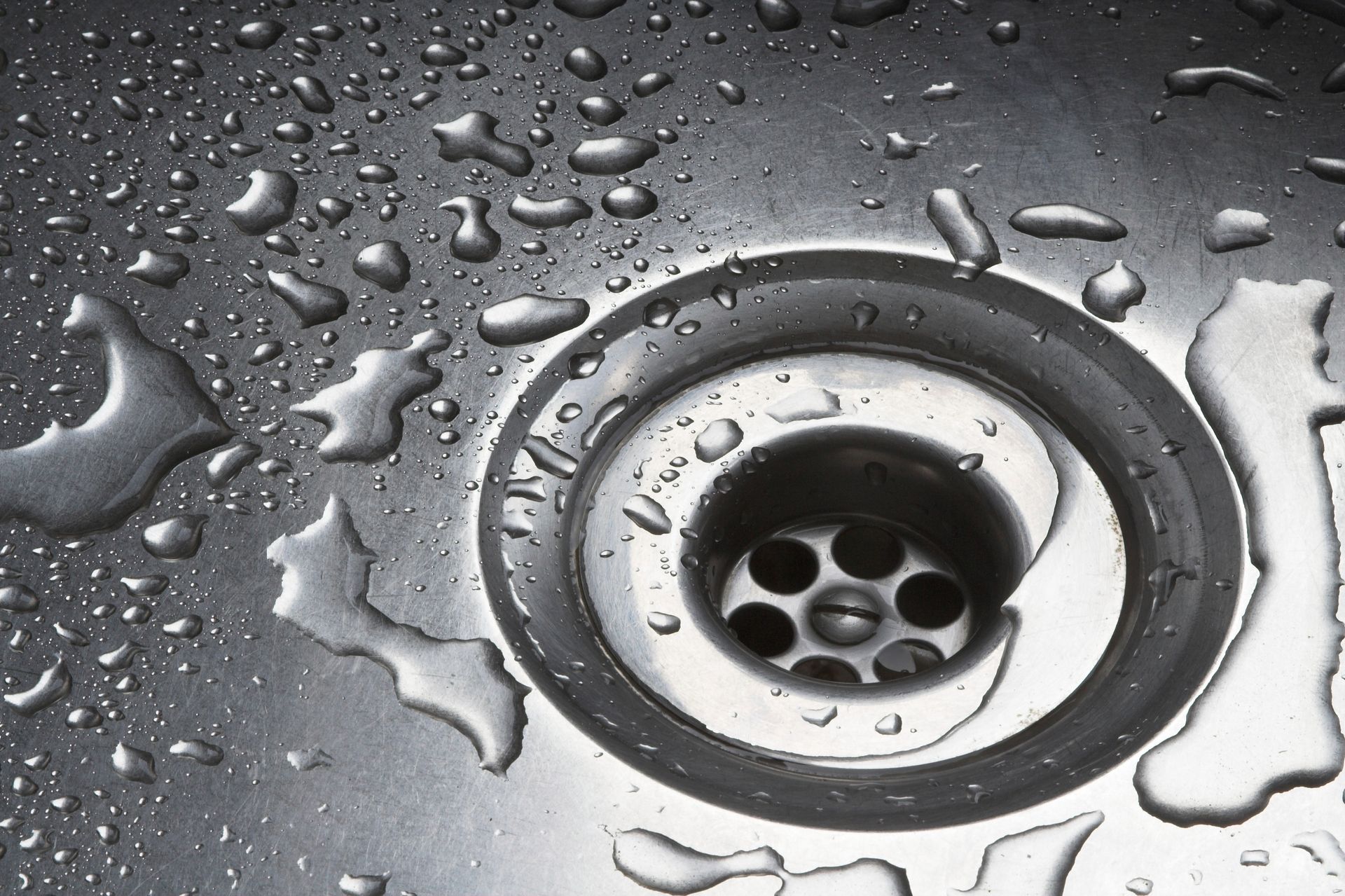 Stainless steel sink with water droplets surrounding the drain.