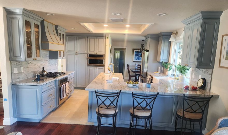 Blue-gray kitchen with island and granite countertops. Includes cabinets, stove, and three bar stools.