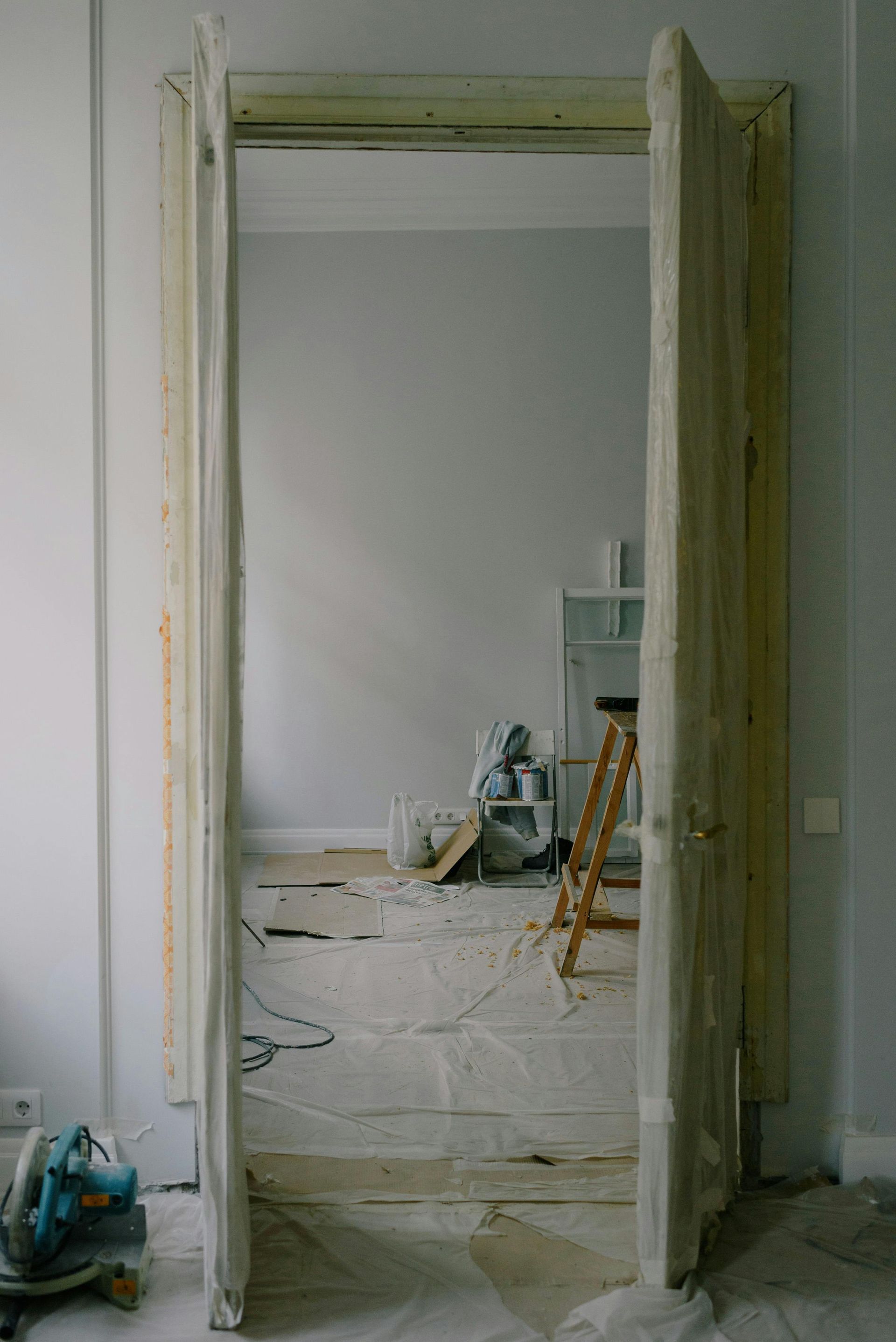 Doorway during renovation with tools, ladder, and room with gray walls.