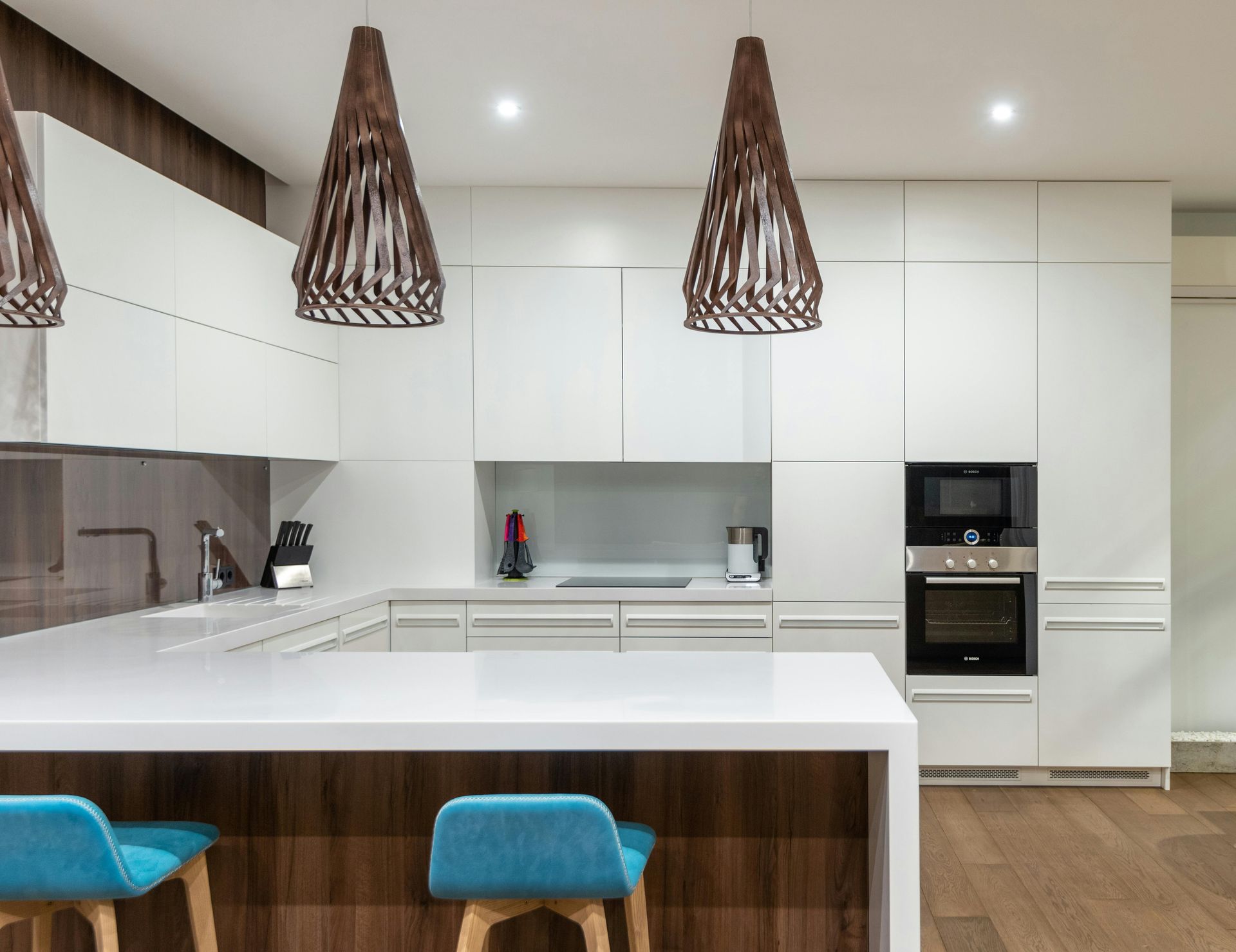 Modern white kitchen with wooden accents, island with blue stools, and pendant lights.