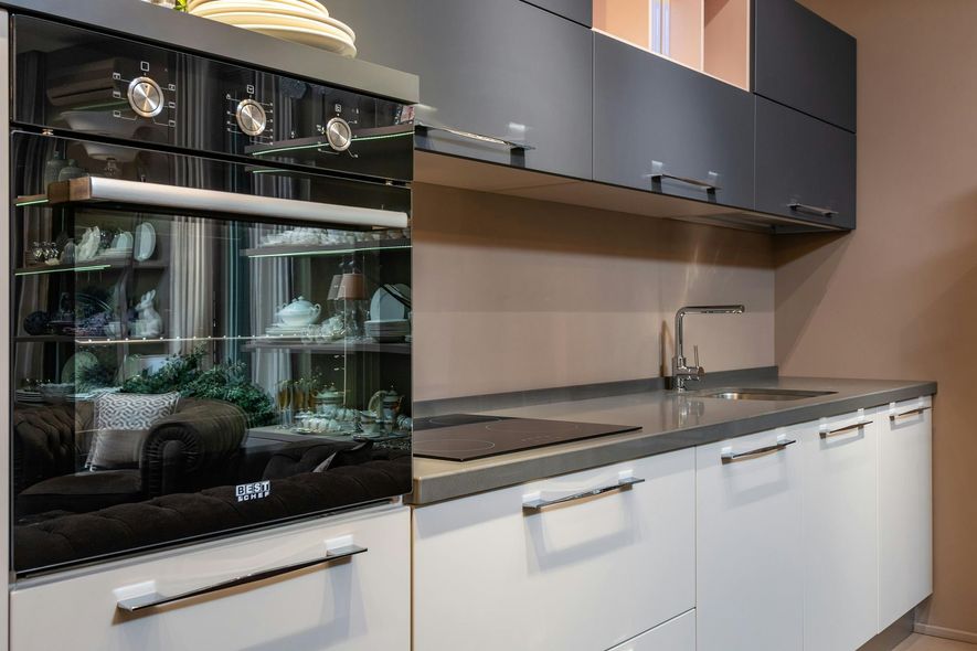 Modern kitchen with black oven, white cabinets, gray countertop, and dark upper cabinets.
