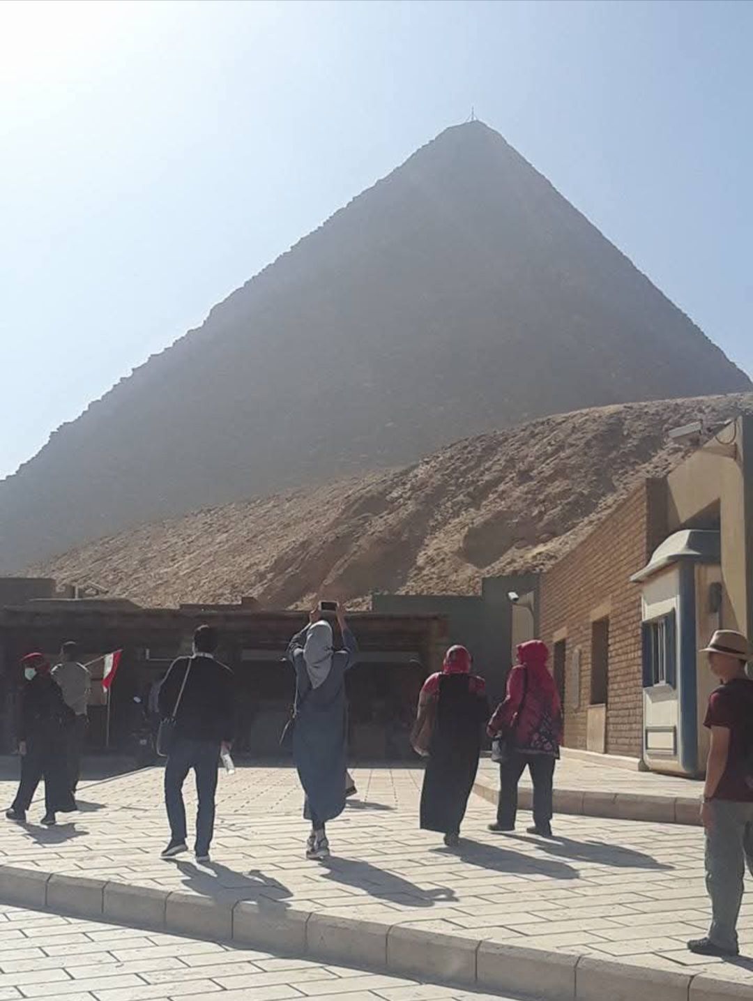 A group of people are walking in front of a pyramid.