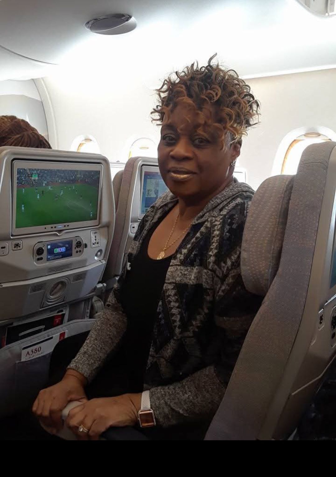 A woman is sitting on an airplane in front of a television.