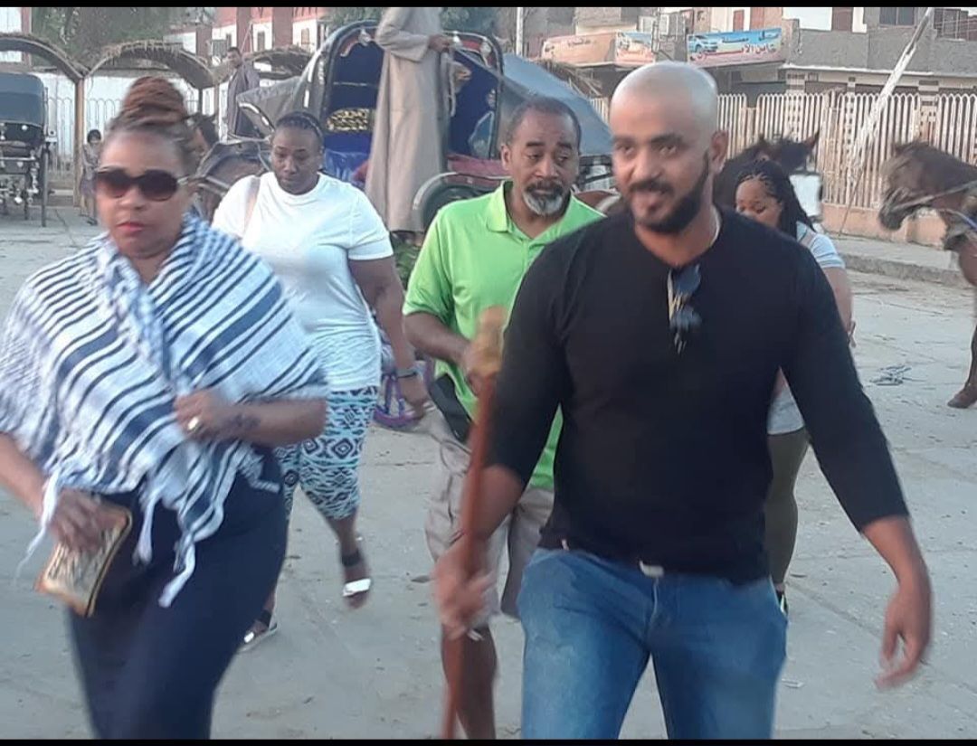 A group of people are walking down a street with a horse drawn carriage in the background.