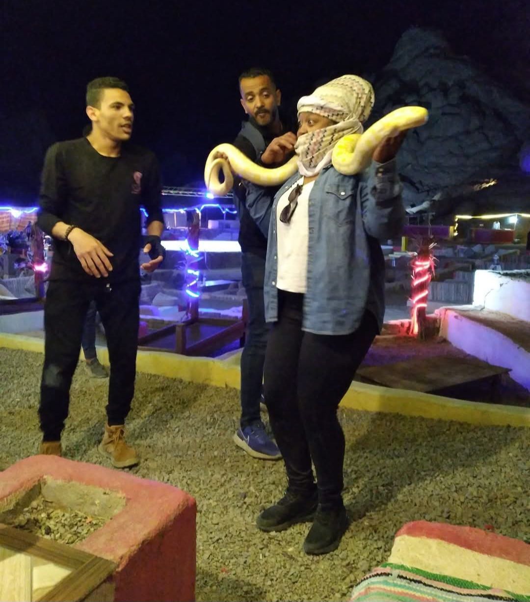 A woman is holding a snake while two men look on