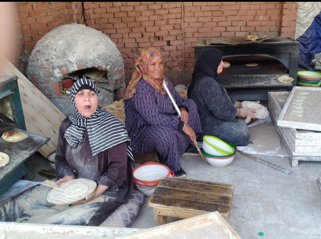 A group of women are sitting in front of a brick oven making food.
