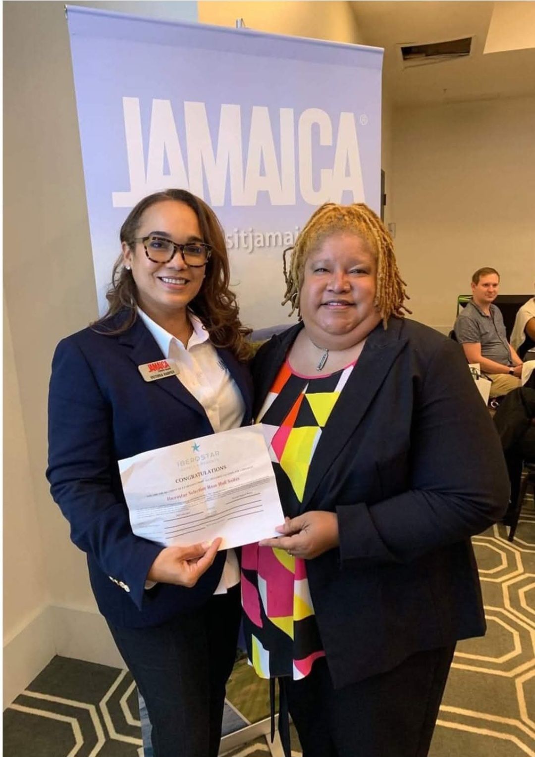 Two women are posing for a picture in front of a sign that says jamaica