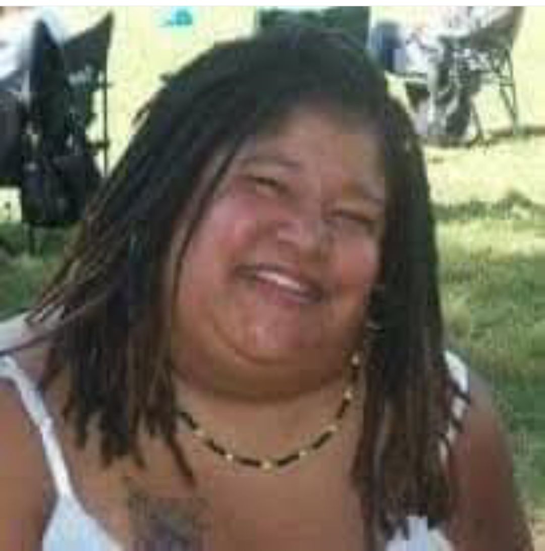 A woman with dreadlocks is smiling and wearing a necklace.