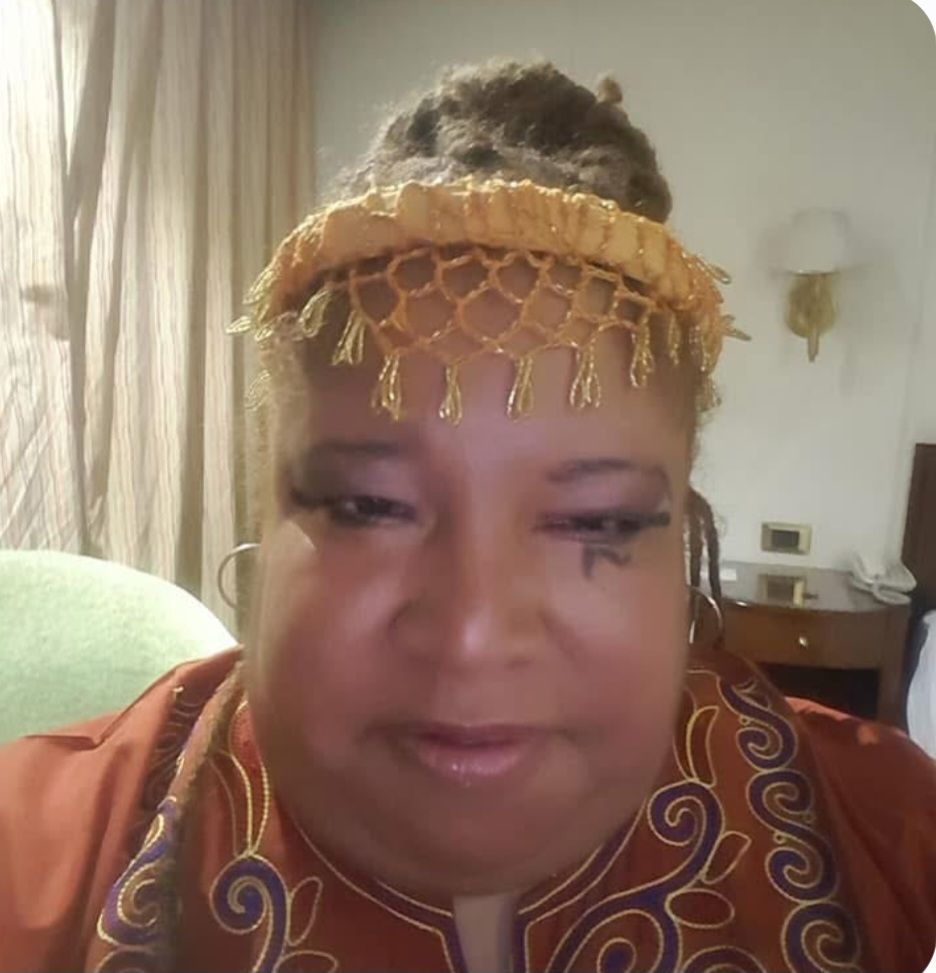 A woman is wearing a headband and earrings and has a tattoo on her face.