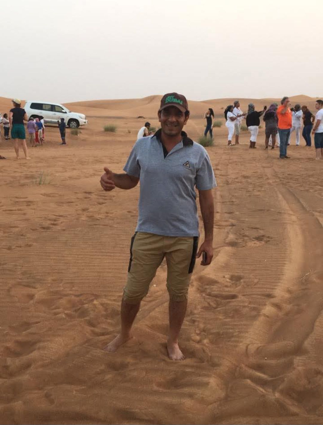 A man is standing in the middle of a desert giving a thumbs up